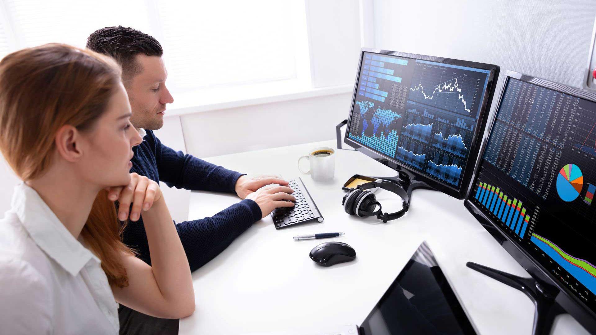 Two people from the DevOps Team sit in front of two monitors