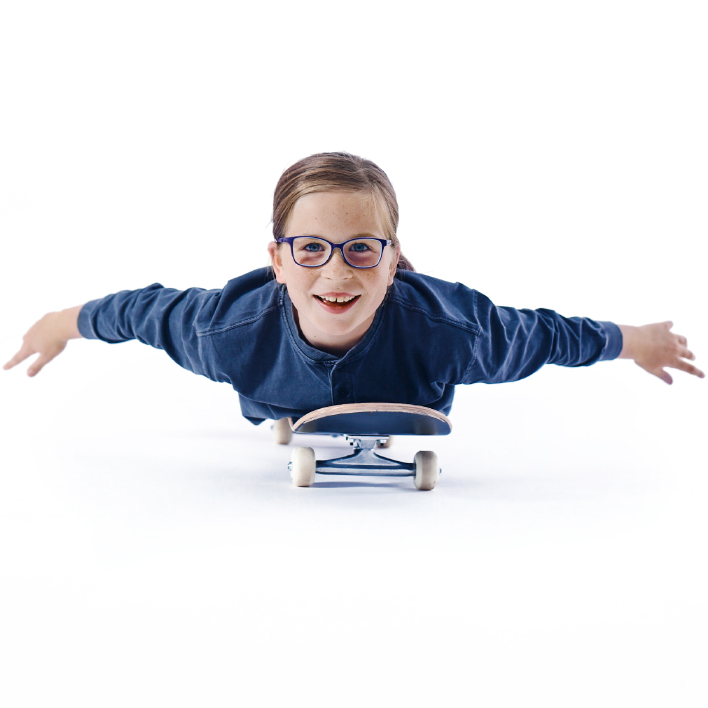 Ein kleines Mädchen mit Brille liegt flach auf einem Skateboard.