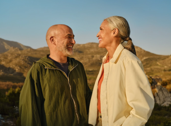An older couple smiling at each other outdoors in warm evening light