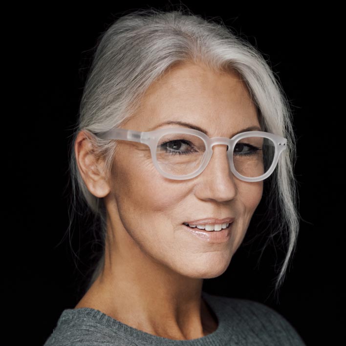 白い縁のZEISS遠近両用スマートライフレンズメガネを装用した、白髪まじりの女性。顔の造りとフレームの数値を表示する、顔の幾何学的な走査。