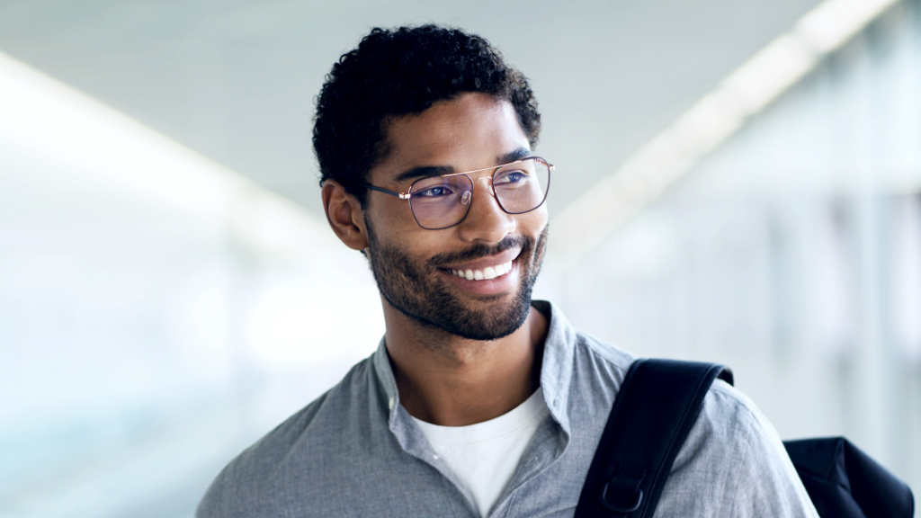 어깨에 배낭을 메고 미소 짓는 젊은 남성이 자이스 스마트라이프 디지털 안경을 착용하고 옆을 보고 있다.
